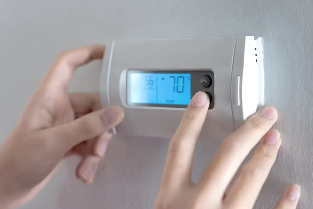 Hands adjusting a digital wall thermostat